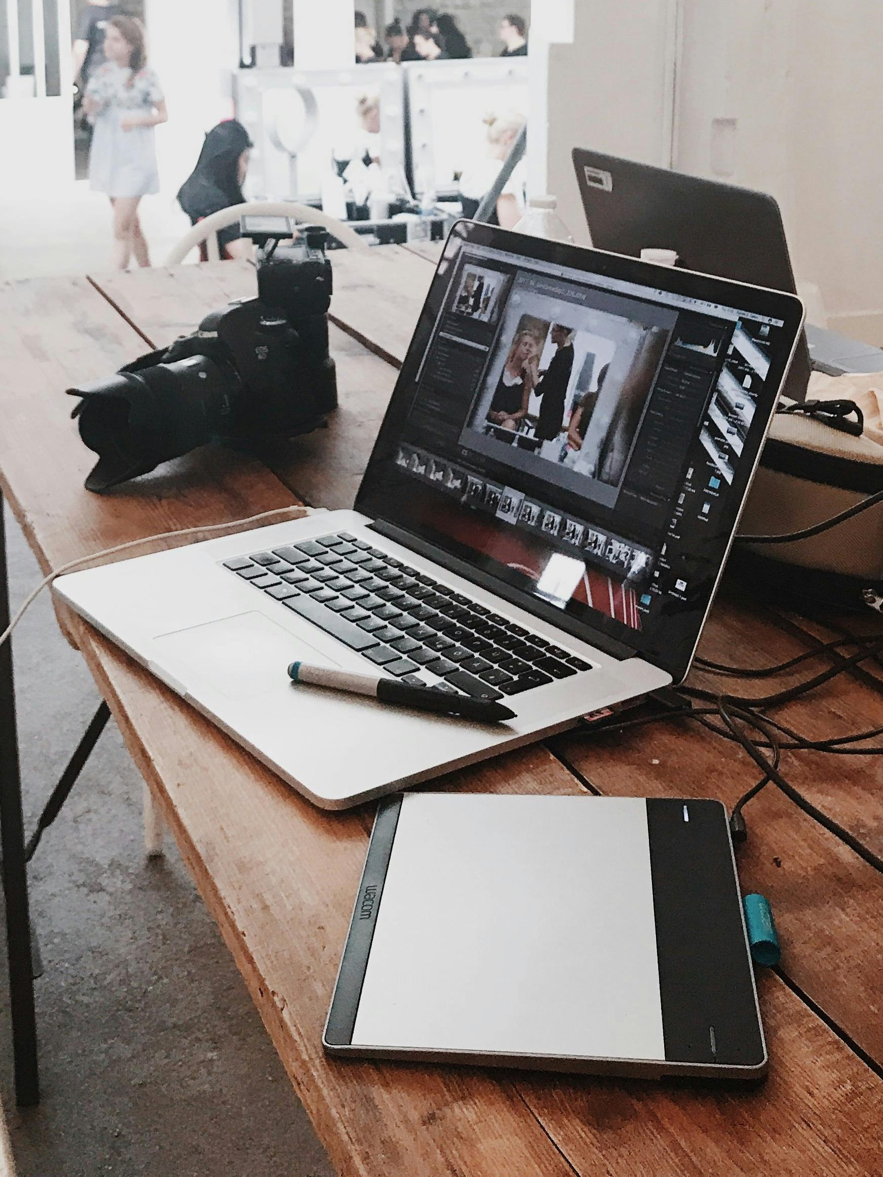 A bright, modern workspace featuring laptops, a camera, and a drawing tablet in an indoor office.